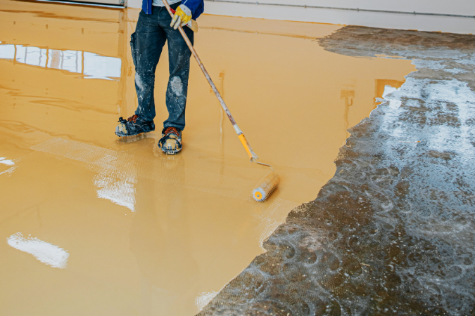 An epoxy screed floor being laid by an installer in a warehouse who is comparing the differences between this and a concrete floor.