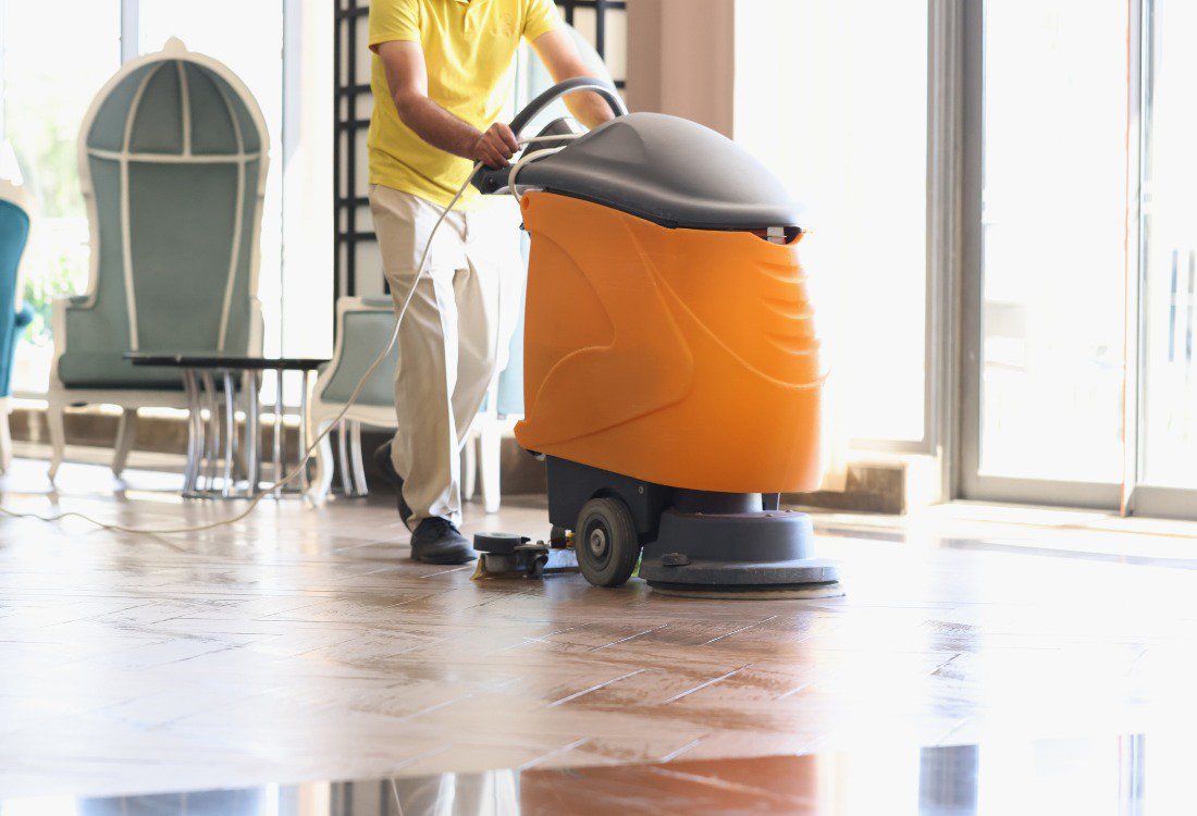 A hotel worker cleaning a tiled hotel lobby floor.