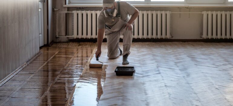 A worker spreading yellow epoxy resin over wood floor​s.