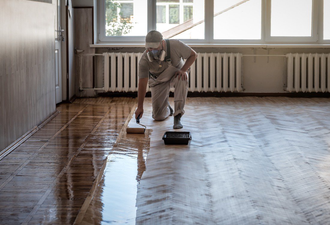 A worker spreading yellow epoxy resin over wood floor​s.
