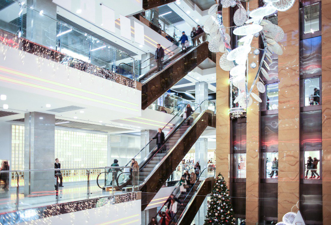 An aerial view of a modern shopping center entrance leading into a multi-level car park, showcasing different types of durable flooring surfaces suitable for high-traffic commercial and parking environments.