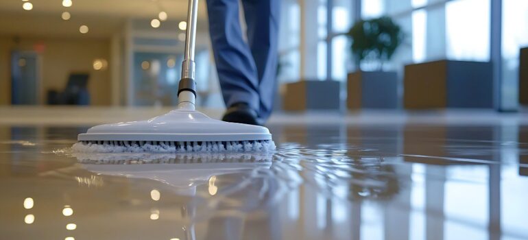 Worker cleaning and polishing a shiny commercial floor with professional equipment in a modern building, representing durable methyl methacrylate flooring.